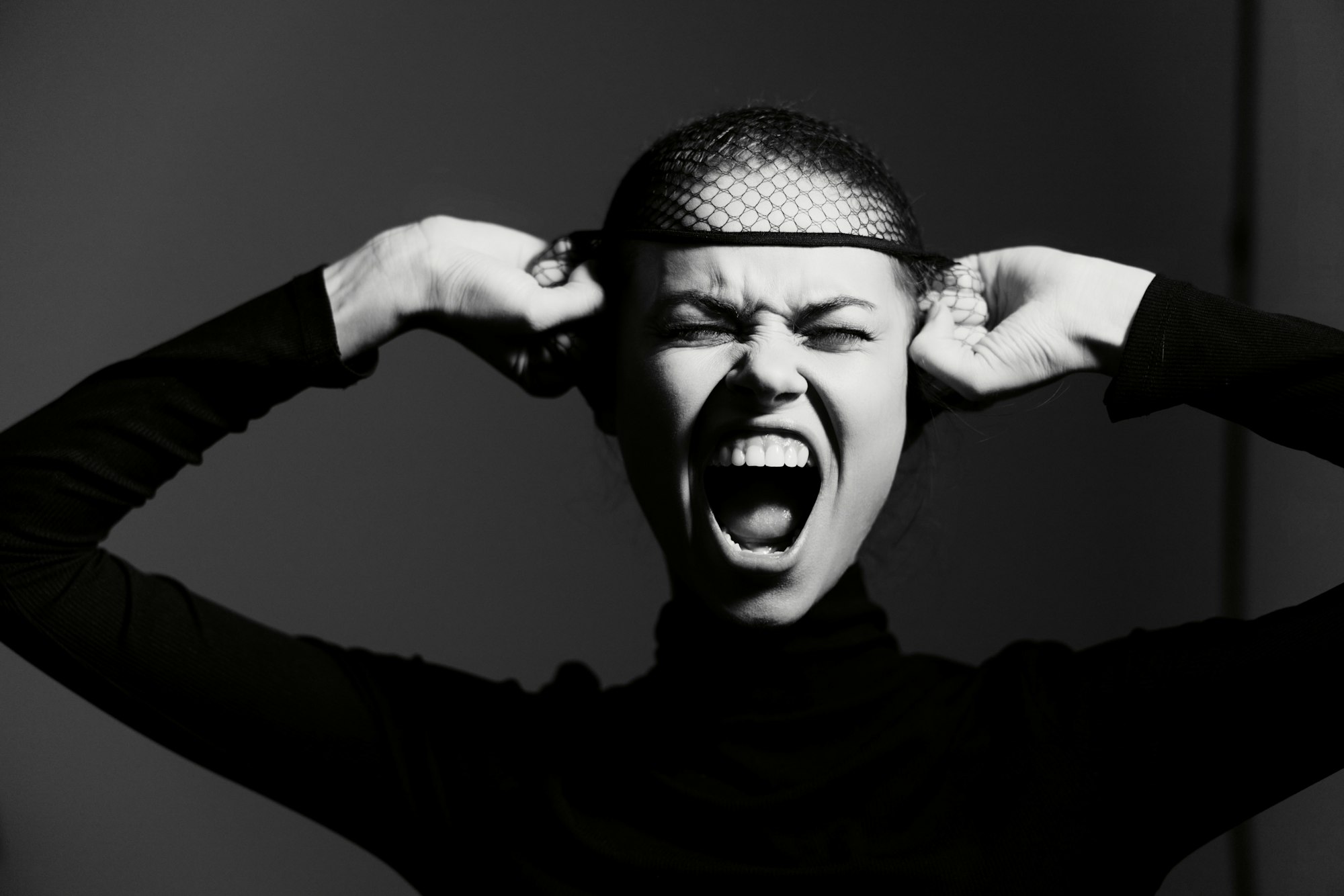 Emotional young woman expressing frustration, wearing a black turtleneck and fishnet headpiece